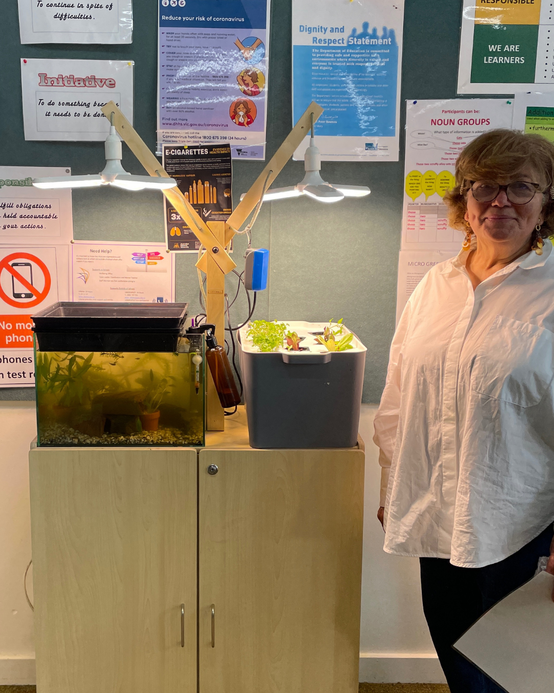 A teacher standing beside her classroom Farmwall system with aquarium and seedlings