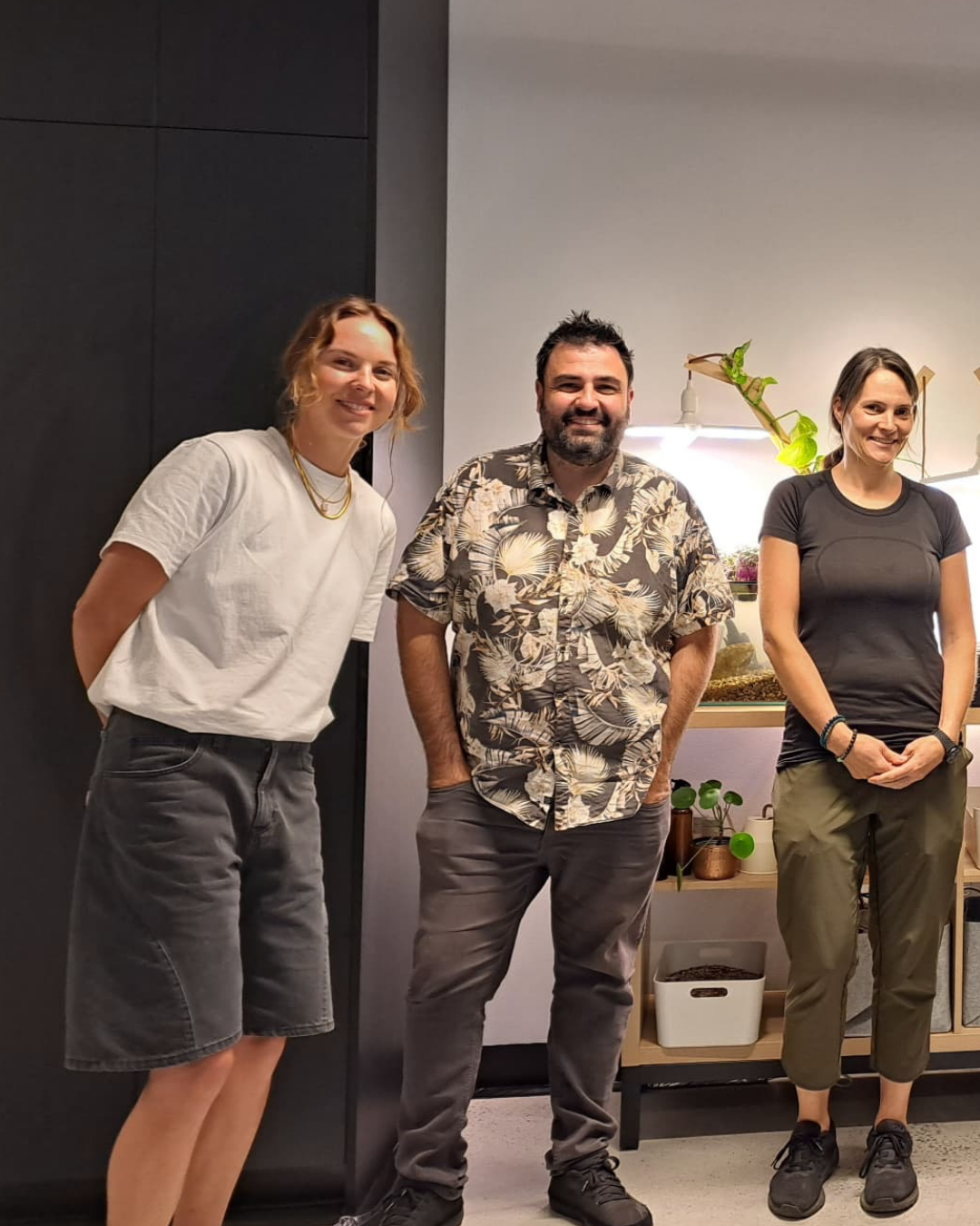 Three smiling people standing beside a Farmwall system with an aquarium and growing tray